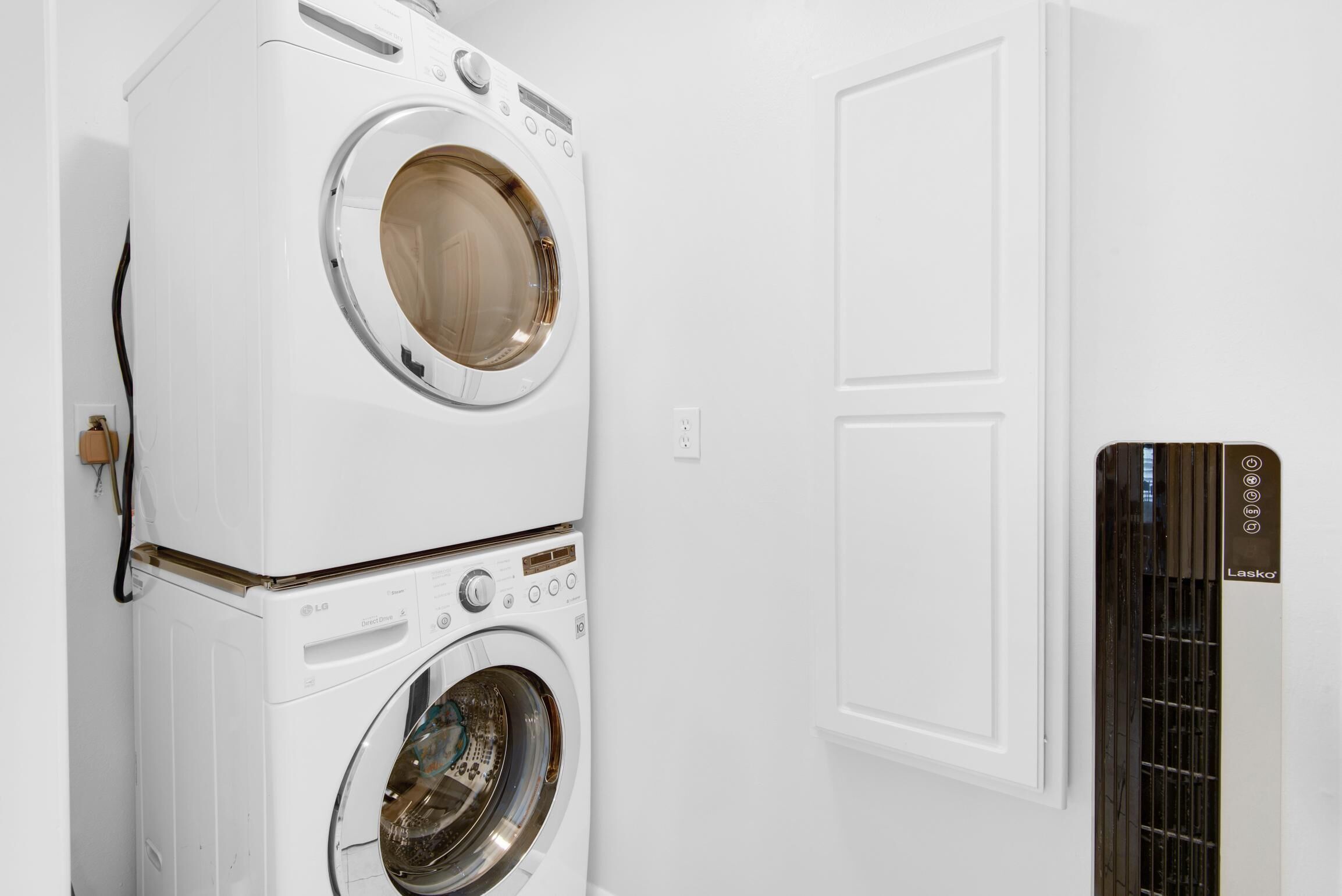 Un appareil combiné lave-linge et sèche-linge, de type « superpos é », se trouve dans une pièce aux murs blancs, avec une porte.