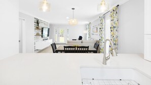 A modern kitchen with white countertops, a dining area with a white table and chairs, and a large window providing natural light. - Summerhouse Townhomes #5 (Miramar Beach)
