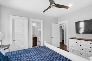 A bedroom with a bed, a ceiling fan, a TV, and white doors leading to other rooms. - Stay Anchored (Miramar Beach)