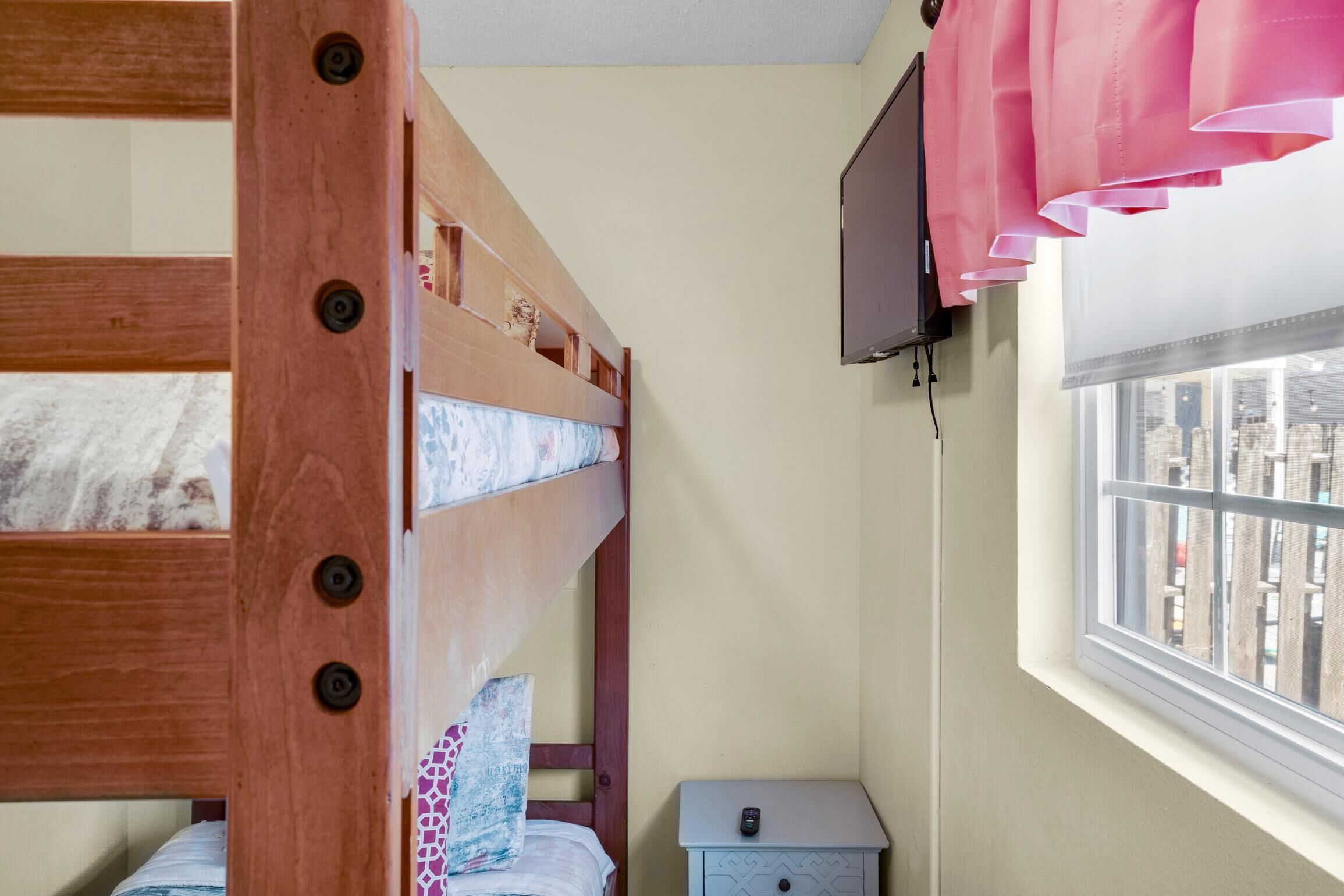 Ein Schlafraum mit Etagenbetten, einem an der Wand befestigten Fernseher und einem Fenster mit Jalousien.