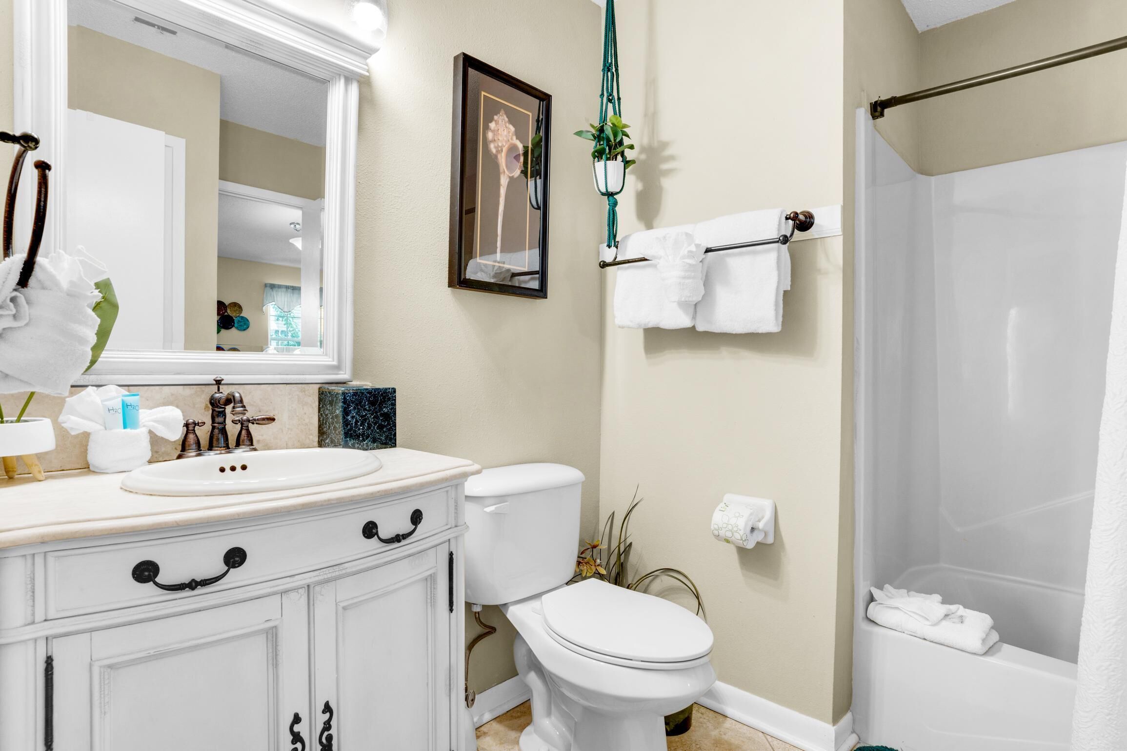 A bathroom with a white sink, toilet, and bathtub. There is a mirror, a towel rack, and a hanging plant.