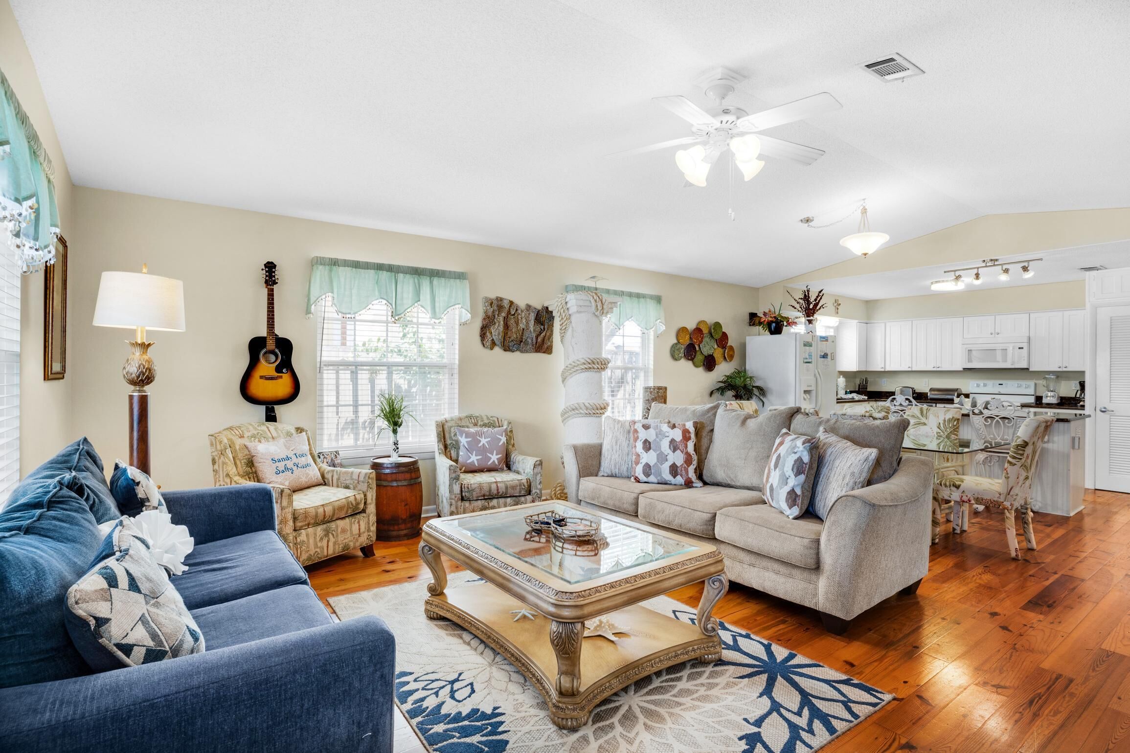 Amplia sala de estar con un sofá azul, una mesa de centro de vidrio y un comedor con una mesa y sillas blancas.