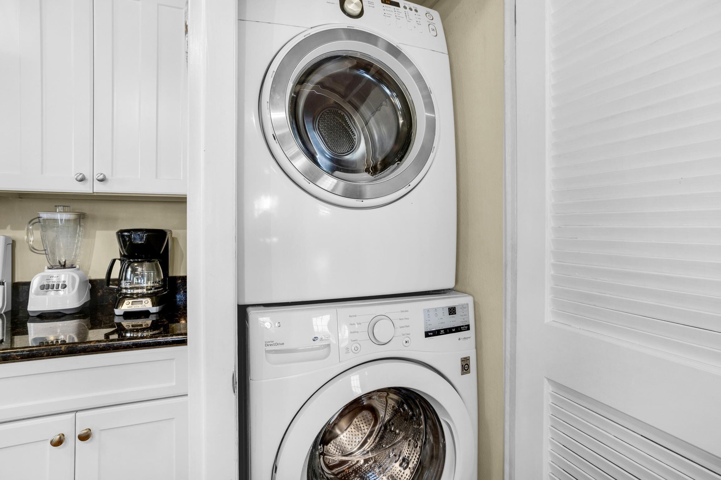 Un appareil combiné lave-linge et sèche-linge, de type « superposé », installé dans une cuisine avec des placards et un plan de travail.