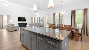 A spacious living area with a large island, a dining table, and a TV mounted on the wall. - Shore Enough (Miramar Beach)