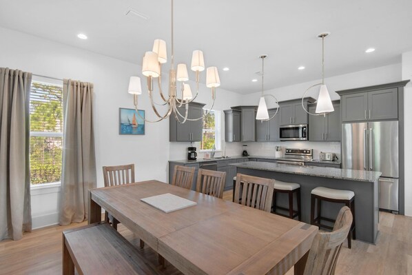 A modern kitchen with grey cabinets, stainless steel appliances, and a wooden dining table with chairs. - Shore Enough (Miramar Beach)