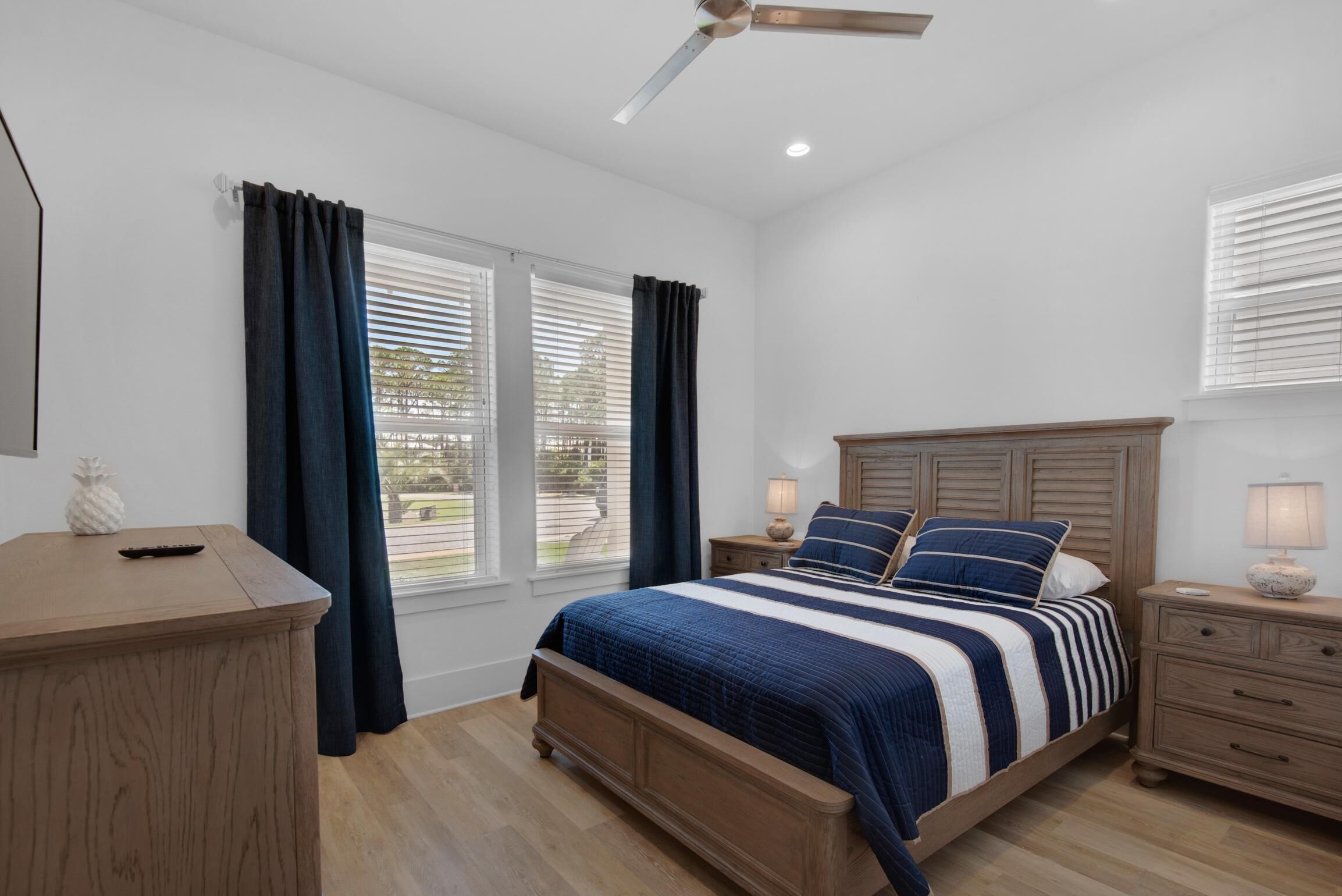 A bedroom with a bed, nightstands, a wooden dresser, and a ceiling fan.
