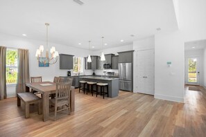 A modern kitchen with a central island, wooden dining table, and bar stools. - Shore Enough (Miramar Beach)