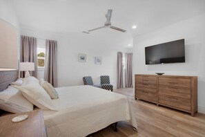 A bedroom with a bed, bedside table, lamp, ceiling fan, TV, and wooden dresser. - Shore Enough (Miramar Beach)