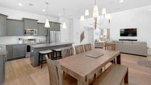 A modern kitchen with grey cabinets, stainless steel appliances, and a central island with bar stools. - Shore Enough (Miramar Beach)