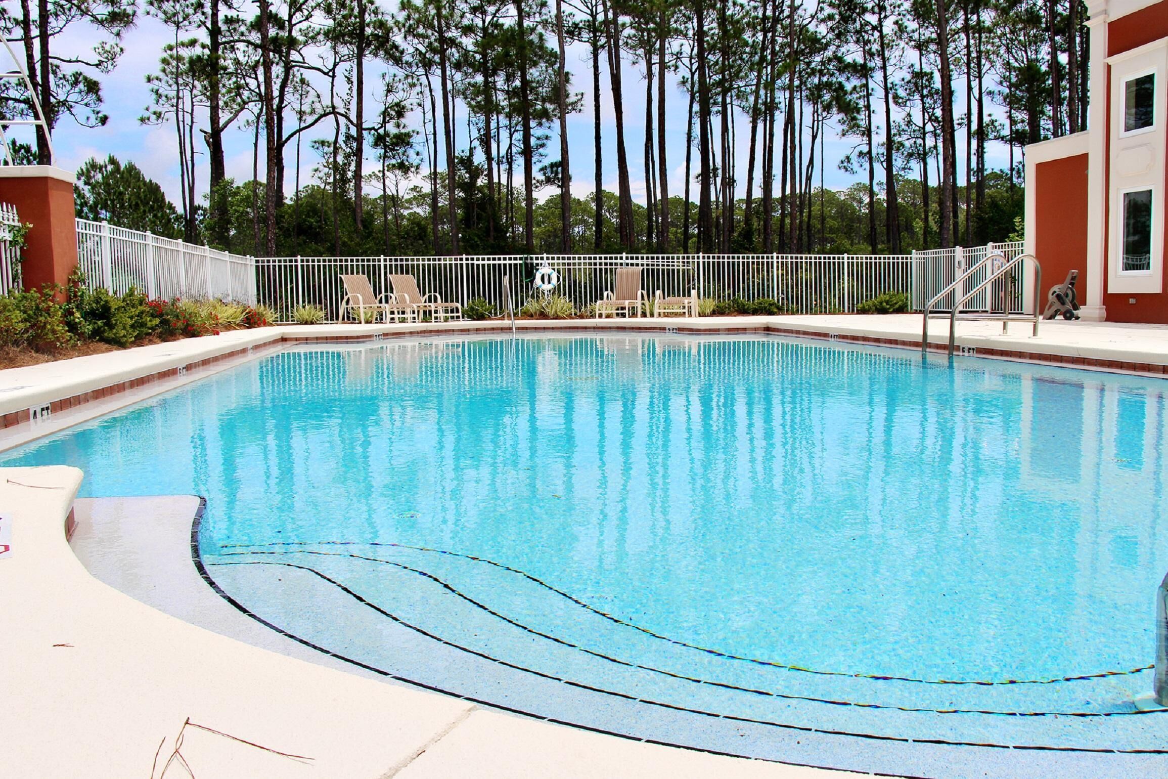 A rectangular swimming pool with a white deck and a white fence surrounding it.