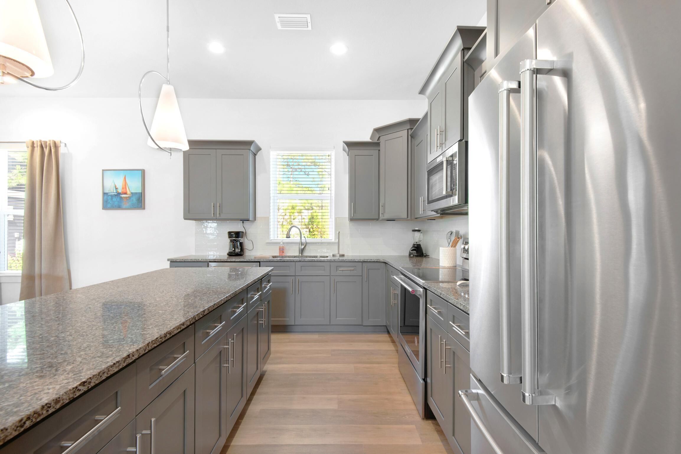 A modern kitchen with grey cabinets, stainless steel appliances, and a granite countertop.
