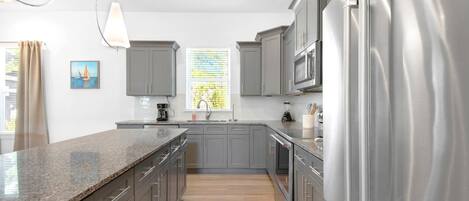 A modern kitchen with grey cabinets, stainless steel appliances, and a granite countertop.