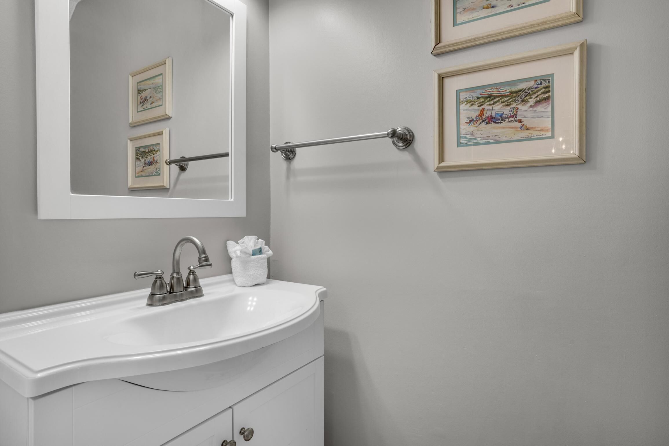 A bathroom with a white sink, a mirror, and two framed pictures on the wall.