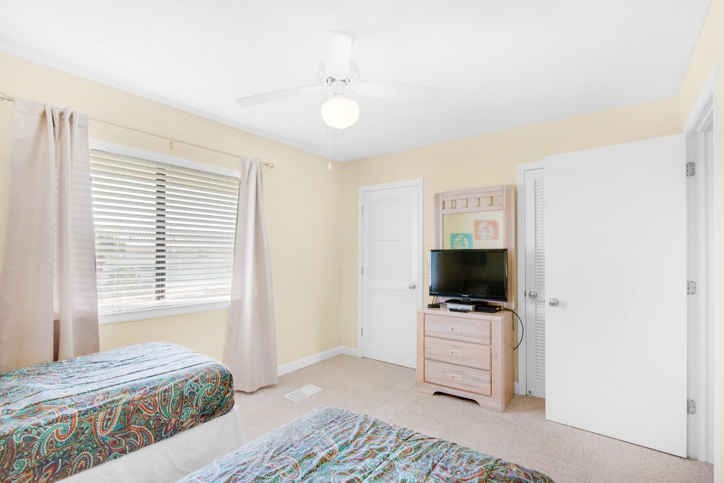 A bedroom with two beds, a ceiling fan, a television on a dresser, and a closet.