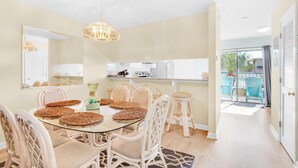 A dining area with a glass table, wicker chairs, and a hanging light fixture.