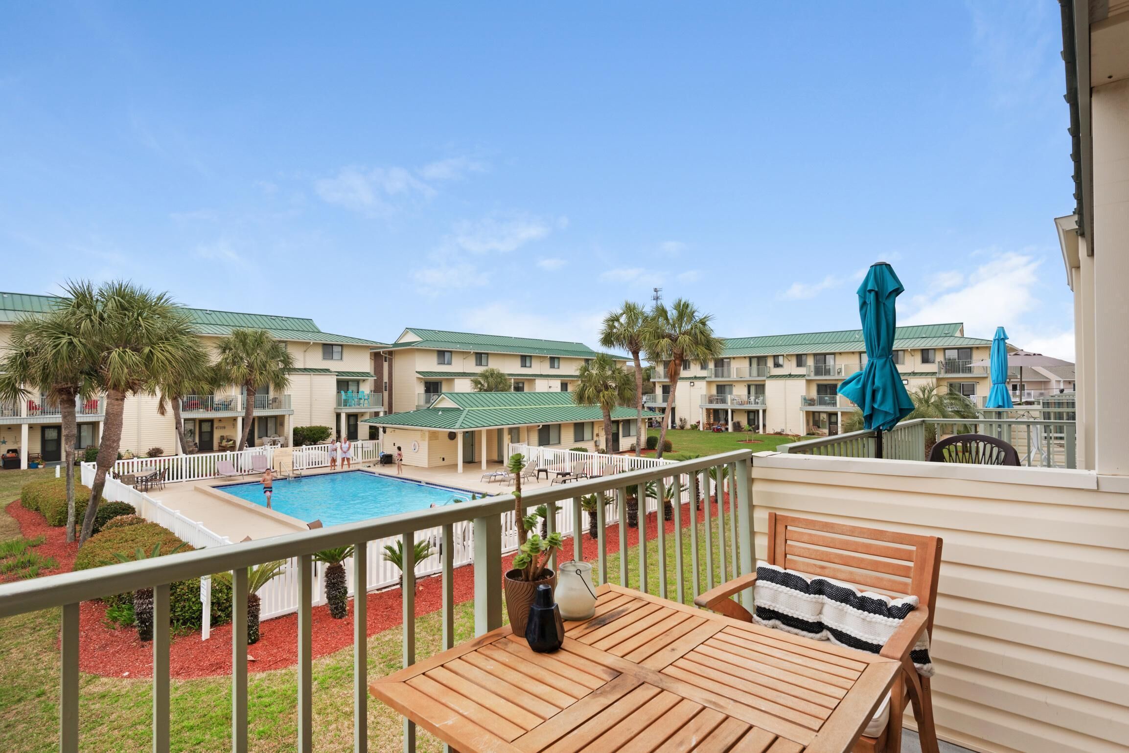 Un balcon avec une table en bois et une vue sur une piscine et les bâtiments de l’hôtel.