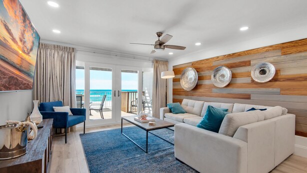 Una sala de estar moderna con un sofá blanco, un sillón azul y una mesa de centro. Hay un ventanal con vista al océano.