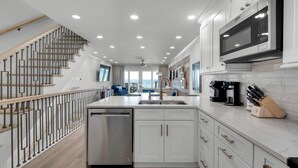 Una cocina moderna con armarios blancos, lavavajillas de acero inoxidable, microondas integrado y cafetera.