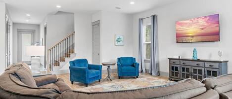 A living room with a brown leather sofa, two blue armchairs, a patterned rug, a cabinet with decorative items, and a sunset painting on the wall.