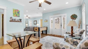 A spacious living room with a glass coffee table, wooden chairs, a sofa, and a foosball table. - Neptune's Nook (Miramar Beach)