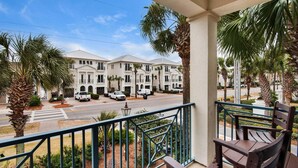 A balcony with a view of a row of white townhouses, palm trees, and a street. - Neptune's Nook (Miramar Beach)