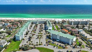An aerial view of a coastal hotel with multiple buildings, parking lots, and a beach in the background. - The Crab Shack (Miramar Beach)
