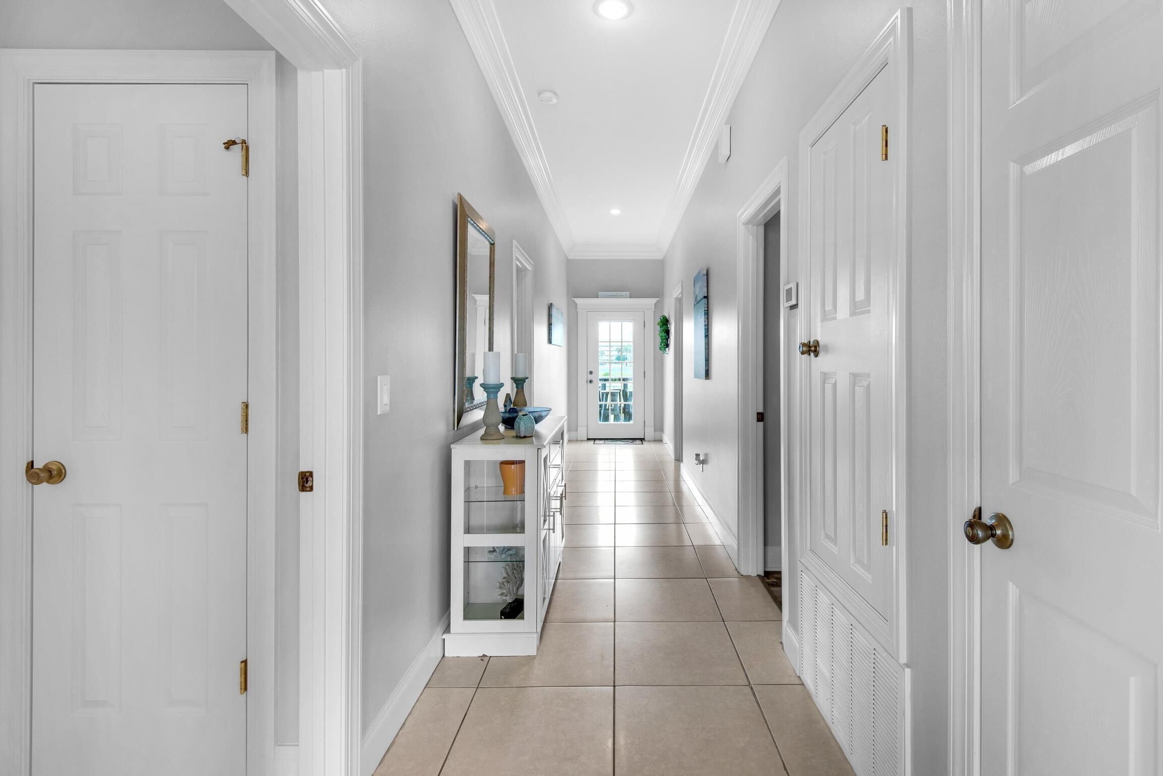 A hallway with white doors, a white console table with decorative items, and a view into a room with a window.
