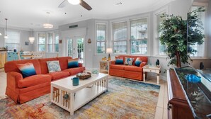A spacious living room with two orange sofas, a white coffee table, and a large fish tank. - The Crab Shack (Miramar Beach)