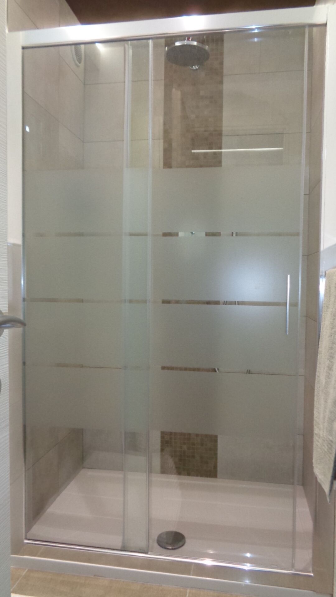 A glass-enclosed shower stall with a tiled floor and a visible drain.