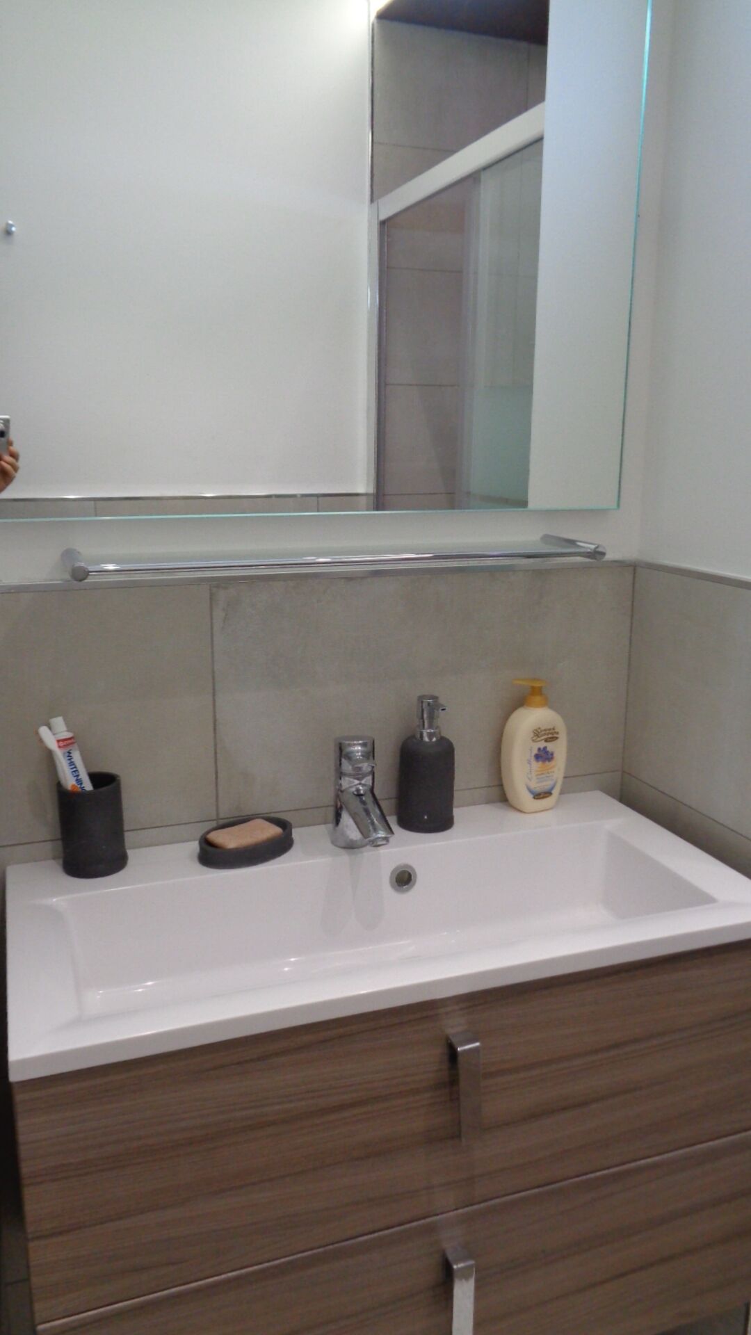 Un bagno con un lavandino bianco, un mobile contenitore in legno scuro e uno specchio sopra il lavandino.