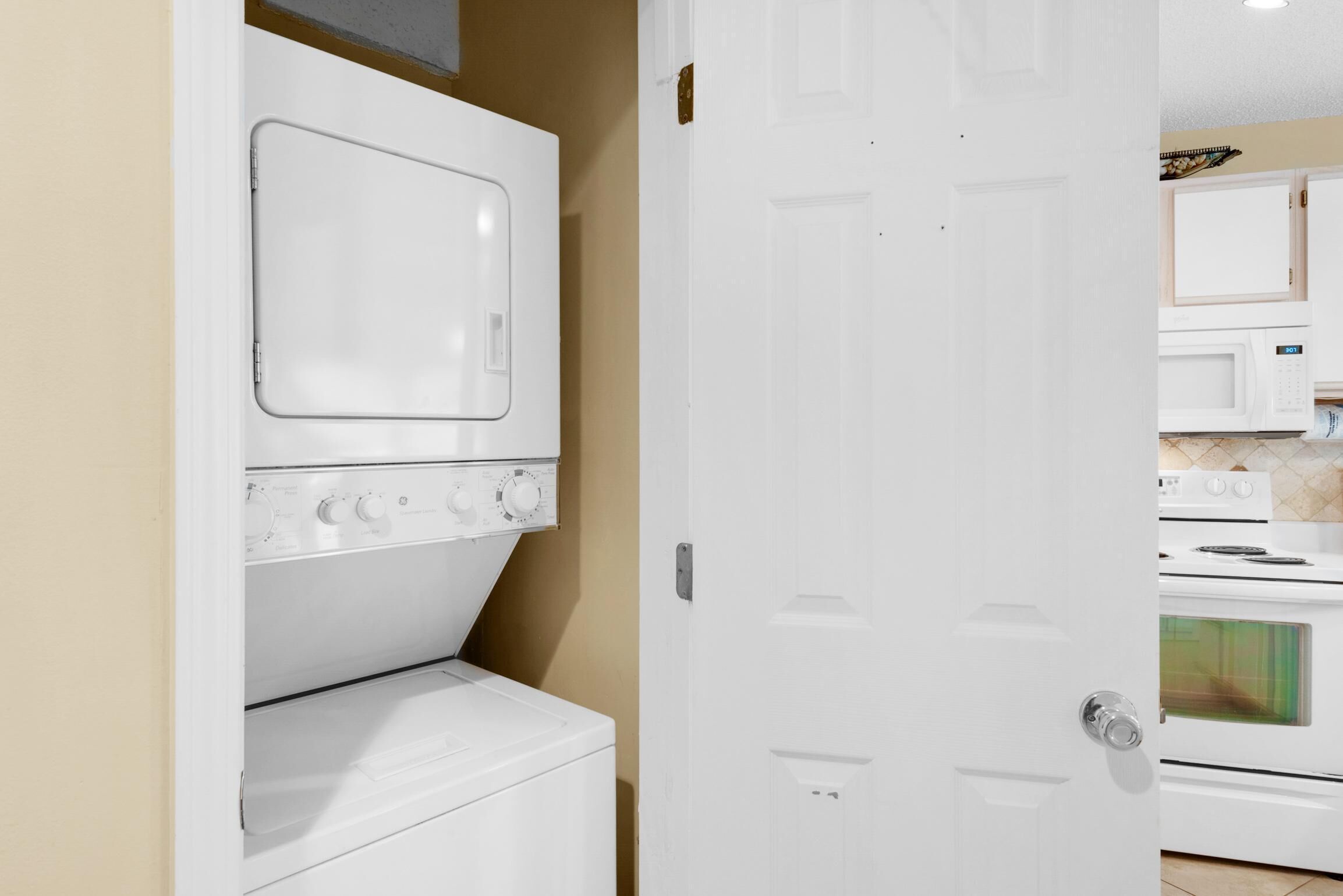 A laundry room with a washer and dryer, a white door, and a kitchen area with a microwave and stove.