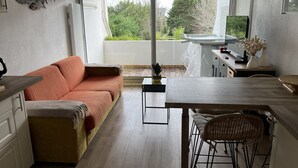 A modern kitchen with a dining area, a sofa, and a view of greenery outside. - Apartment with pool and beach access 2*. No. 31 (Quiberon)