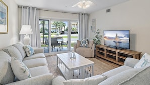 A living room with a sofa, coffee table, TV, and a view of a patio with outdoor furniture. - Maravilla 3102 (Miramar Beach)
