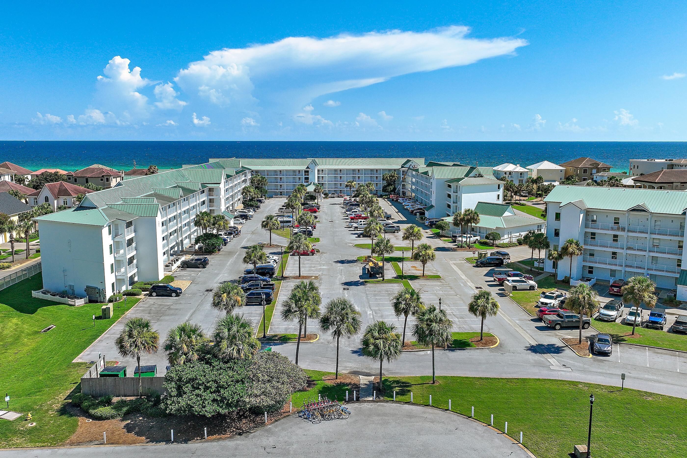 A hotel with a parking lot, multiple buildings, and a view of the ocean.