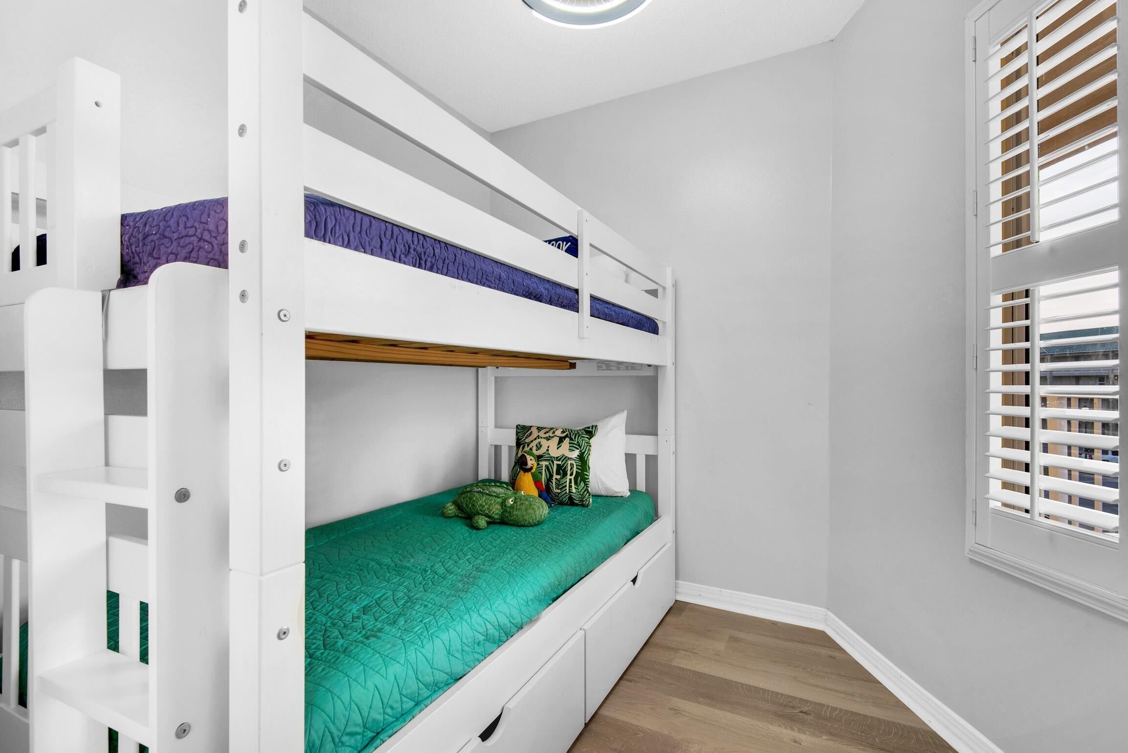 Una cama litera con colchón verde, cabecera blanca y una ventana con persianas.