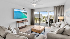 A modern living room with a flat-screen TV, a ceiling fan, and a view of the ocean through large sliding doors. - Maravilla 1309 (Miramar Beach)
