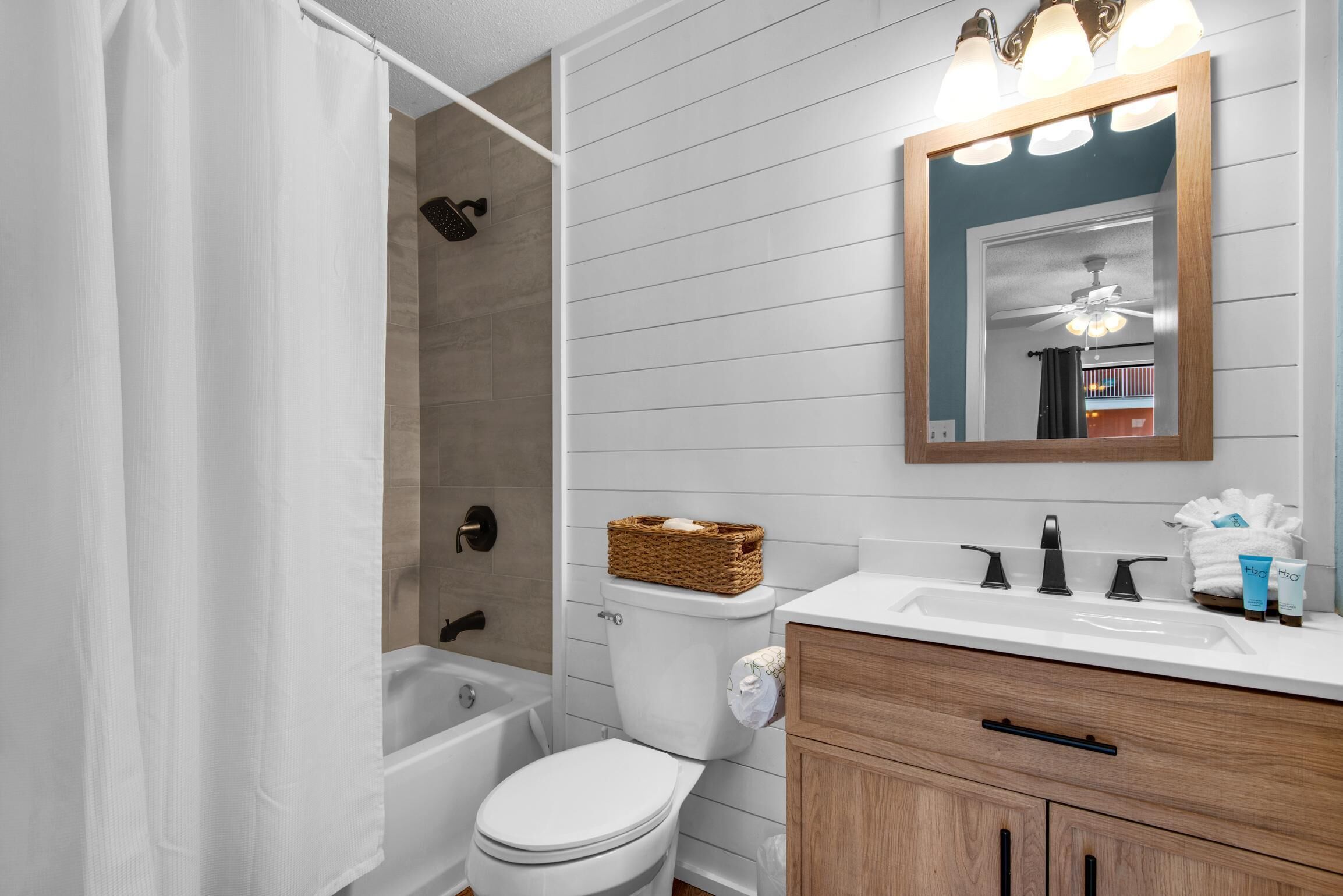 Un bagno con un water bianco, un mobile bagno in legno, uno specchio e una doccia.