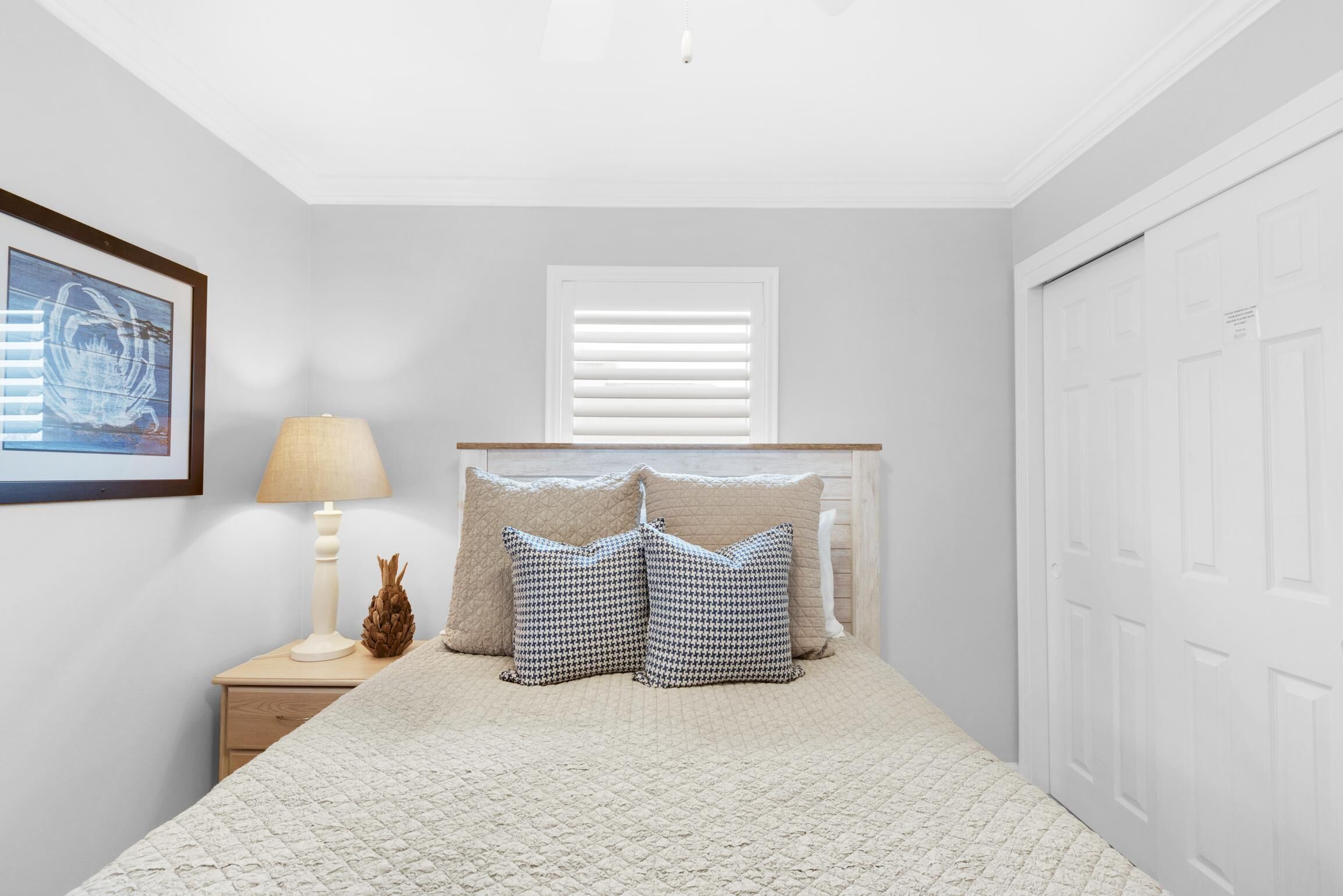 A bedroom with a bed, a nightstand with a lamp, a framed picture, and a window with blinds.