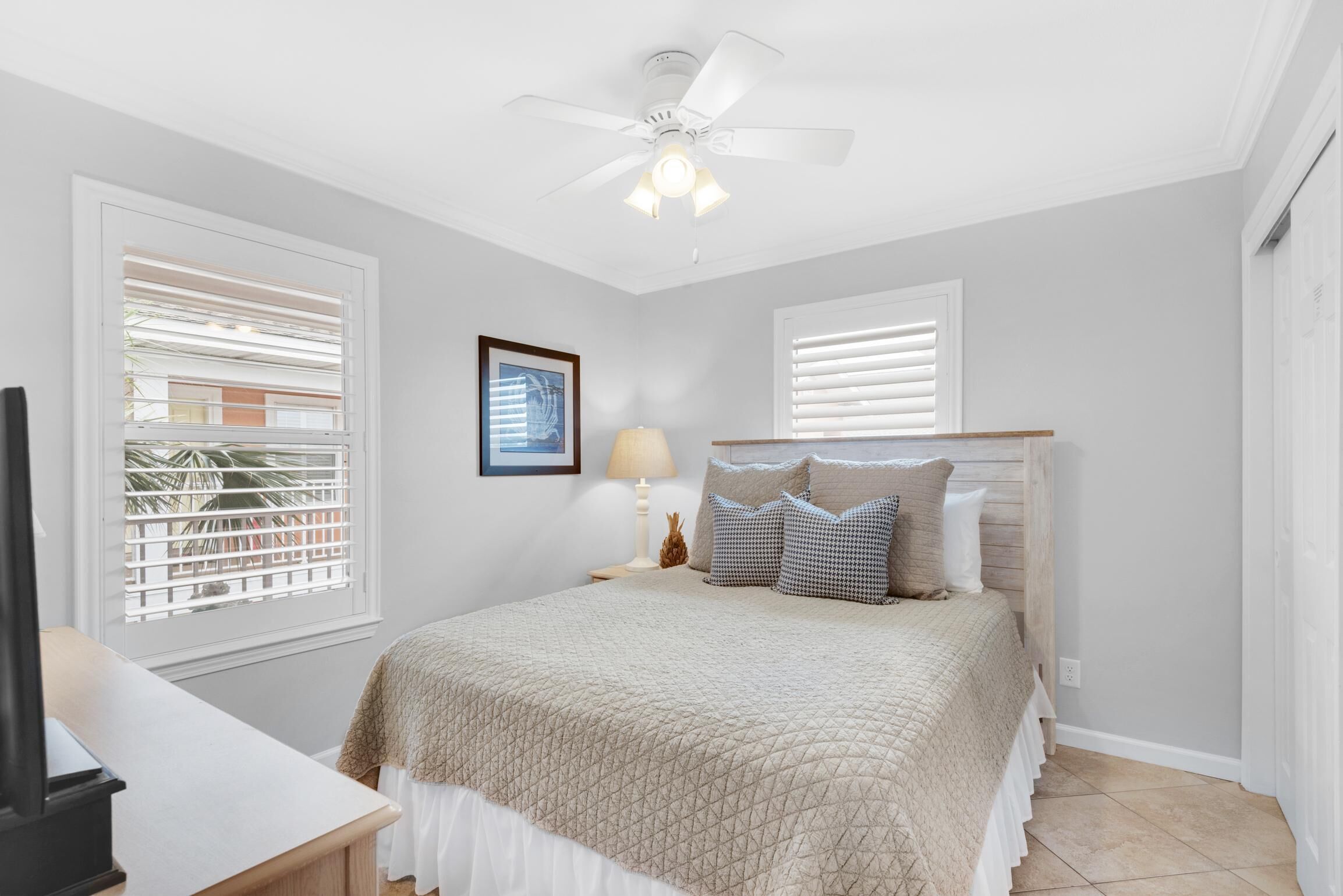 A bedroom with a bed, a ceiling fan, a nightstand with a lamp, and a framed picture on the wall.