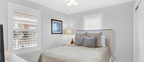 A bedroom with a bed, a ceiling fan, a nightstand with a lamp, and a framed picture on the wall.