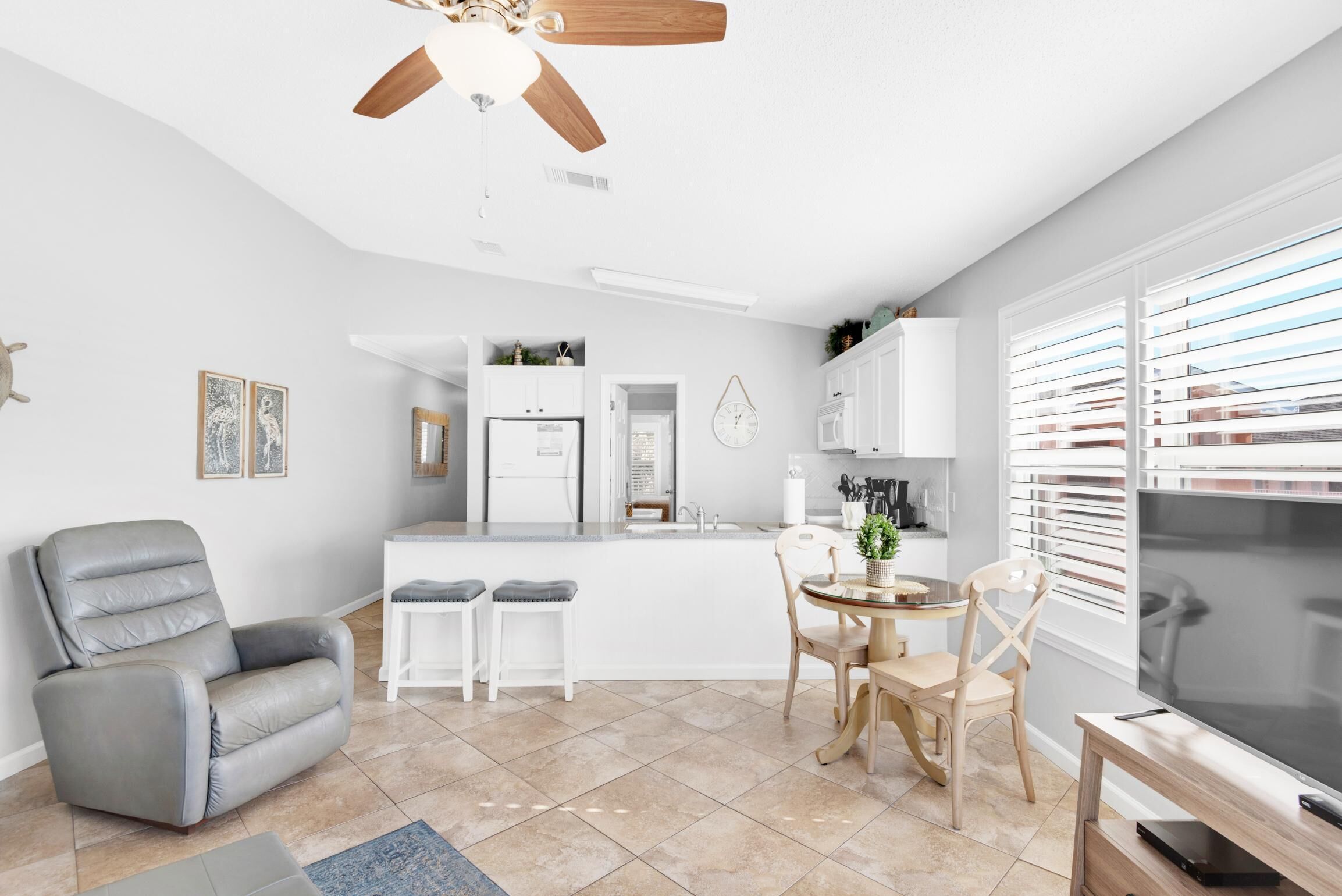 A modern kitchen with white cabinets, a central island, and a dining area with a gray leather chair and wooden table.
