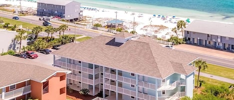 A multi-story hotel with a swimming pool, located near a beach with clear blue waters.