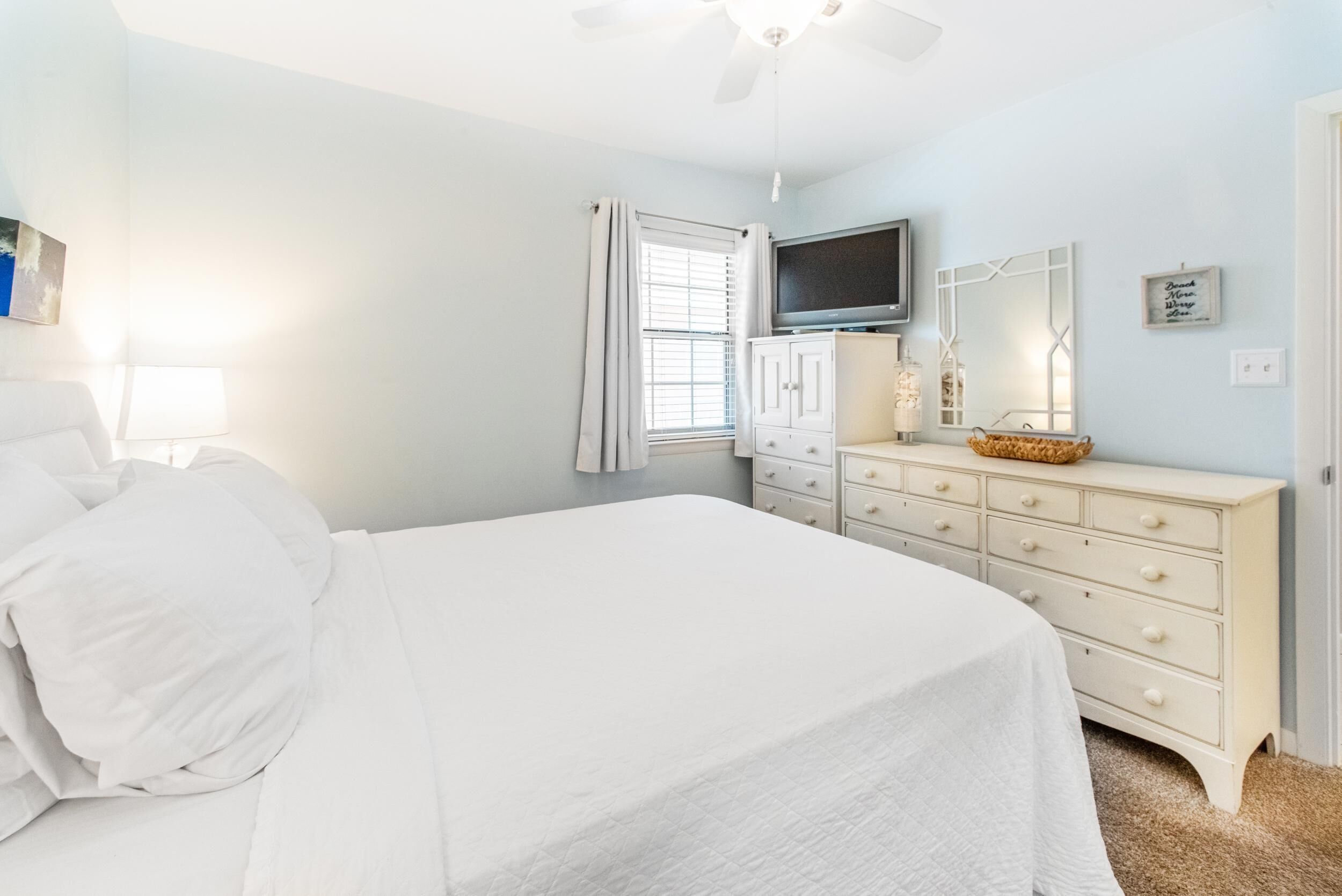 Une chambre à coucher avec un lit, une commode, un téléviseur et un ventilateur de plafond.
