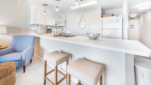 A modern kitchen with white cabinetry, a central island, pendant lighting, and a clock on the wall. - Gulfview I 313 (Miramar Beach)