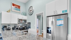 A modern kitchen with white cabinets, a stainless steel refrigerator, a clock, and a coffee maker. - Gulfview II 306 (Miramar Beach)