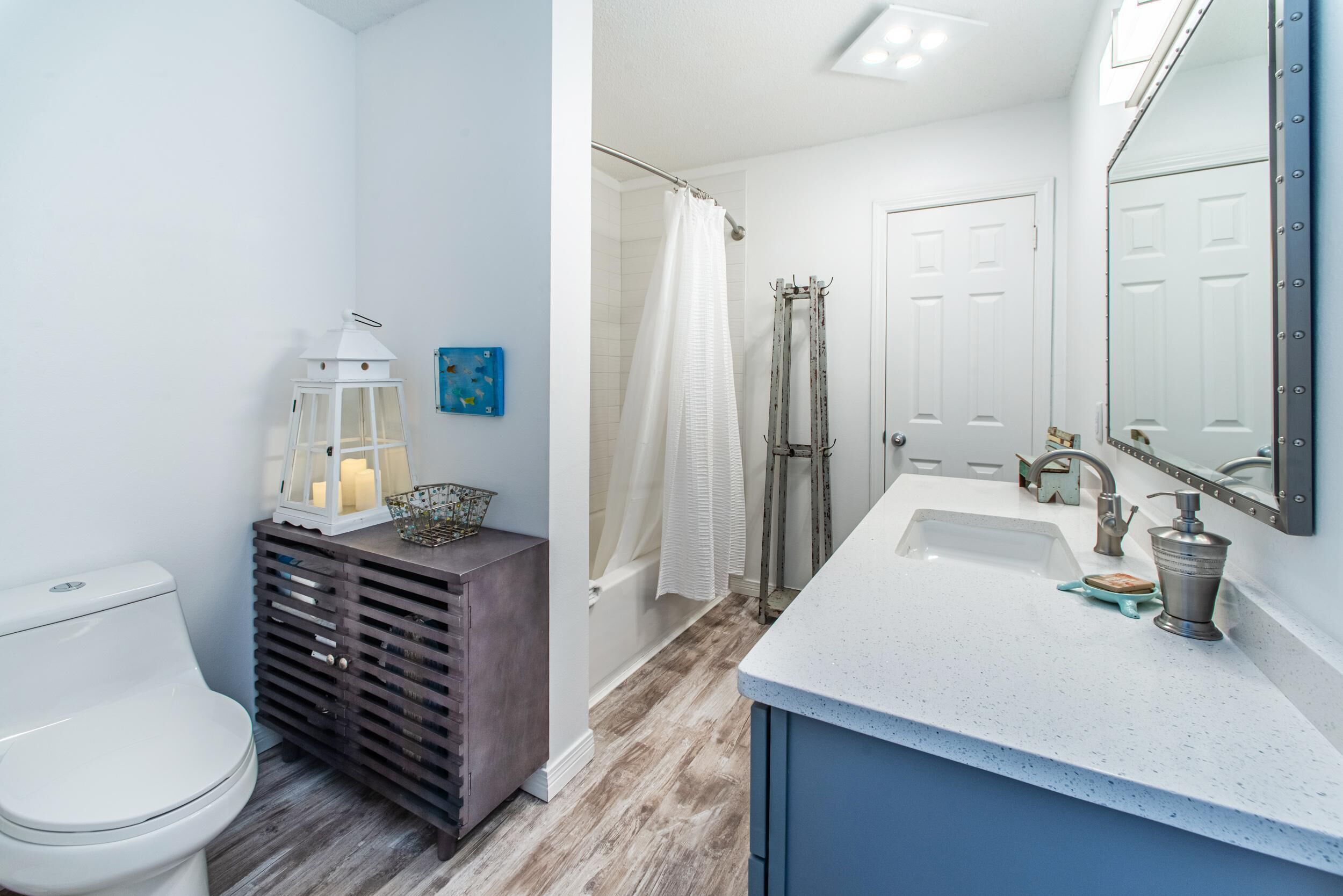 A modern bathroom with a white toilet, a wooden vanity, a white sink with a blue countertop, and a large mirror.
