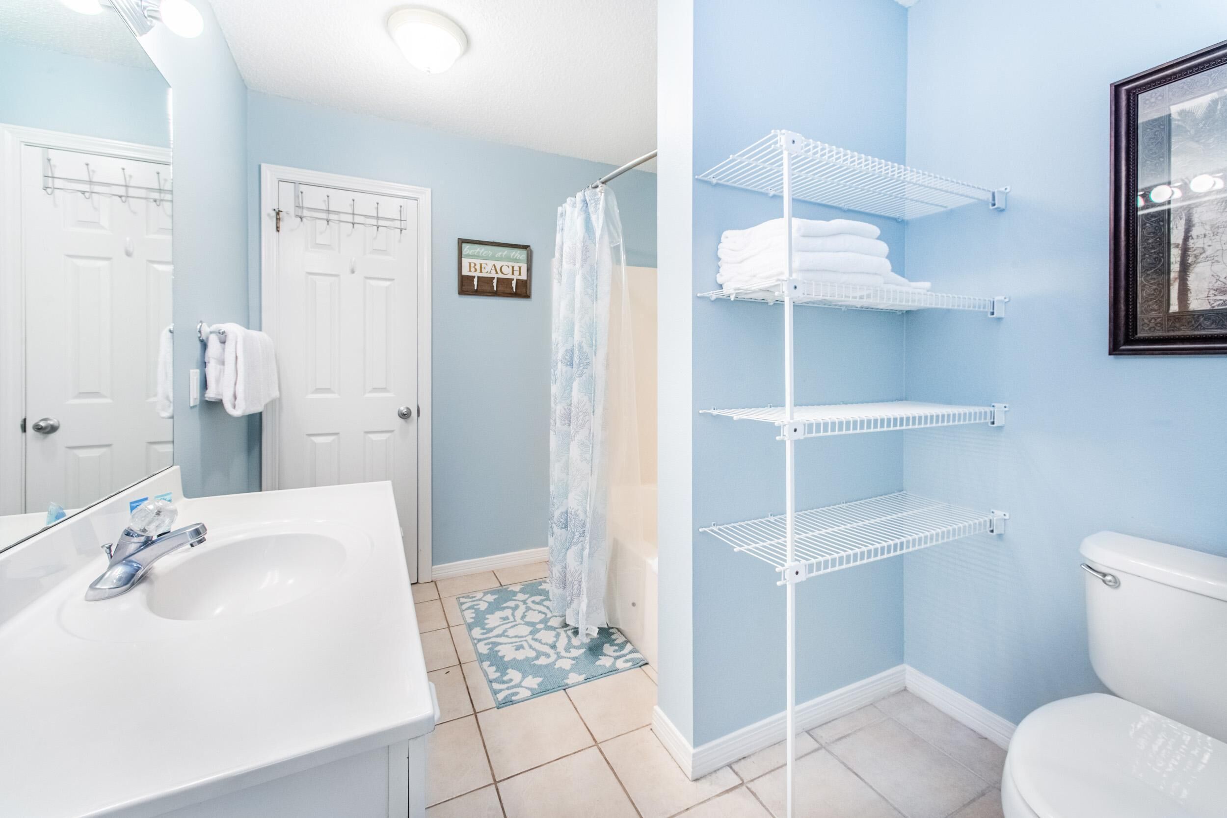 Une salle de bain avec un lavabo blanc, une douche avec une porte en verre et un porte-serviettes avec des serviettes pliées.