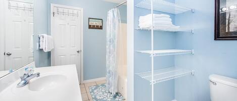 Une salle de bain avec un lavabo blanc, une douche avec une porte en verre et un porte-serviettes avec des serviettes pliées.