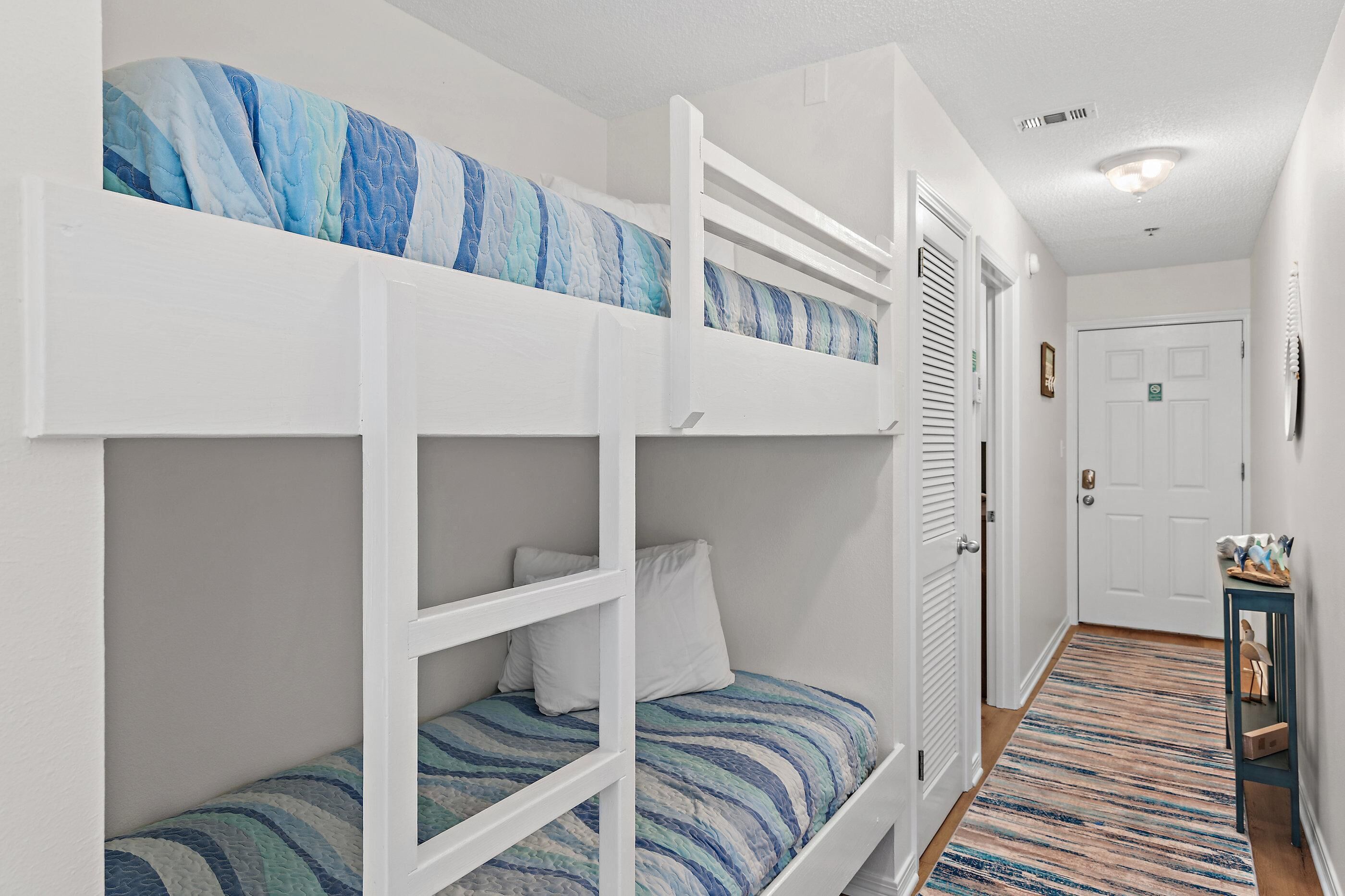 A bunk bed room with a striped bedspread, a white door, and a small table with items on it.