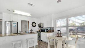 Una cocina moderna con armarios blancos, un refrigerador de acero inoxidable, un microondas y un comedor con una mesa y sillas.